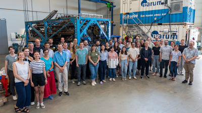 Group photo of the participants of the Ocean Floor Symposium 2024 in front of the seafloor drilling rig MARUM-MeBo 200. Photo: MARUM – Center for Marine Environmental Sciences, University of Bremen; V. Diekamp