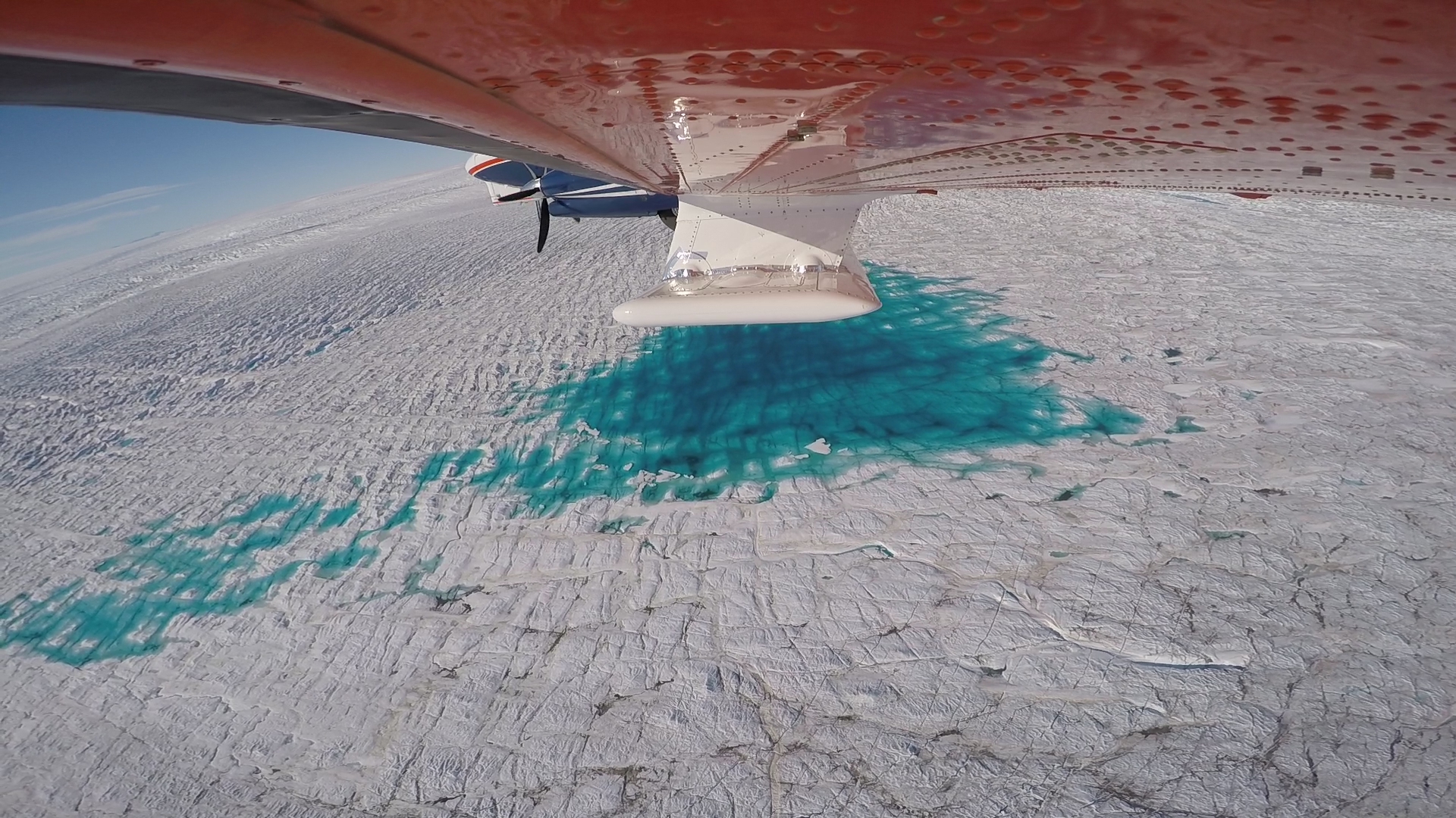 The AWI research aircraft Polar 6 flying over the 79-Degree-North Glacier in Greenland. The photo clearly shows small melt-water lakes on the glacier’s surface. Photo: Alfred-Wegener-Institut