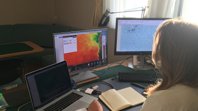 Here I am planning the last sampling stations along the upwelling - open ocean transect off Mauretania. Left screen: actual ocean current speed and direction in the research area, middle: satellite image of research area with upper ocean temperature (blue-green: cold upwelled water, yellow-orange-red: warmer temperatures), right screen: sea map with program to determine the distances (nautical miles) between planned stations. Photo: Gerard Versteegh