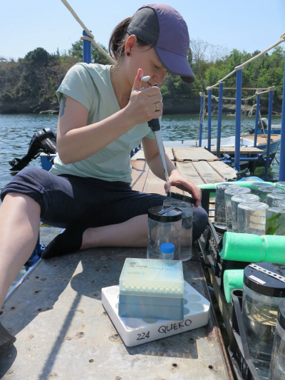 Johanna sitting at a waterside surrounded by lab equipment holding a pipette