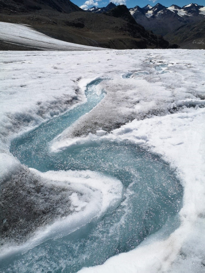 a turquoise channel of water meanders through a landscape of white snow and ice