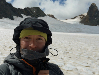 Nina's head covered with two hats in front of a glacial landscape